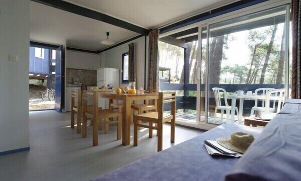 A modern room with a dining area, a balcony with white chairs, and a view of trees. - Sowell LES Cavales (Carcans)