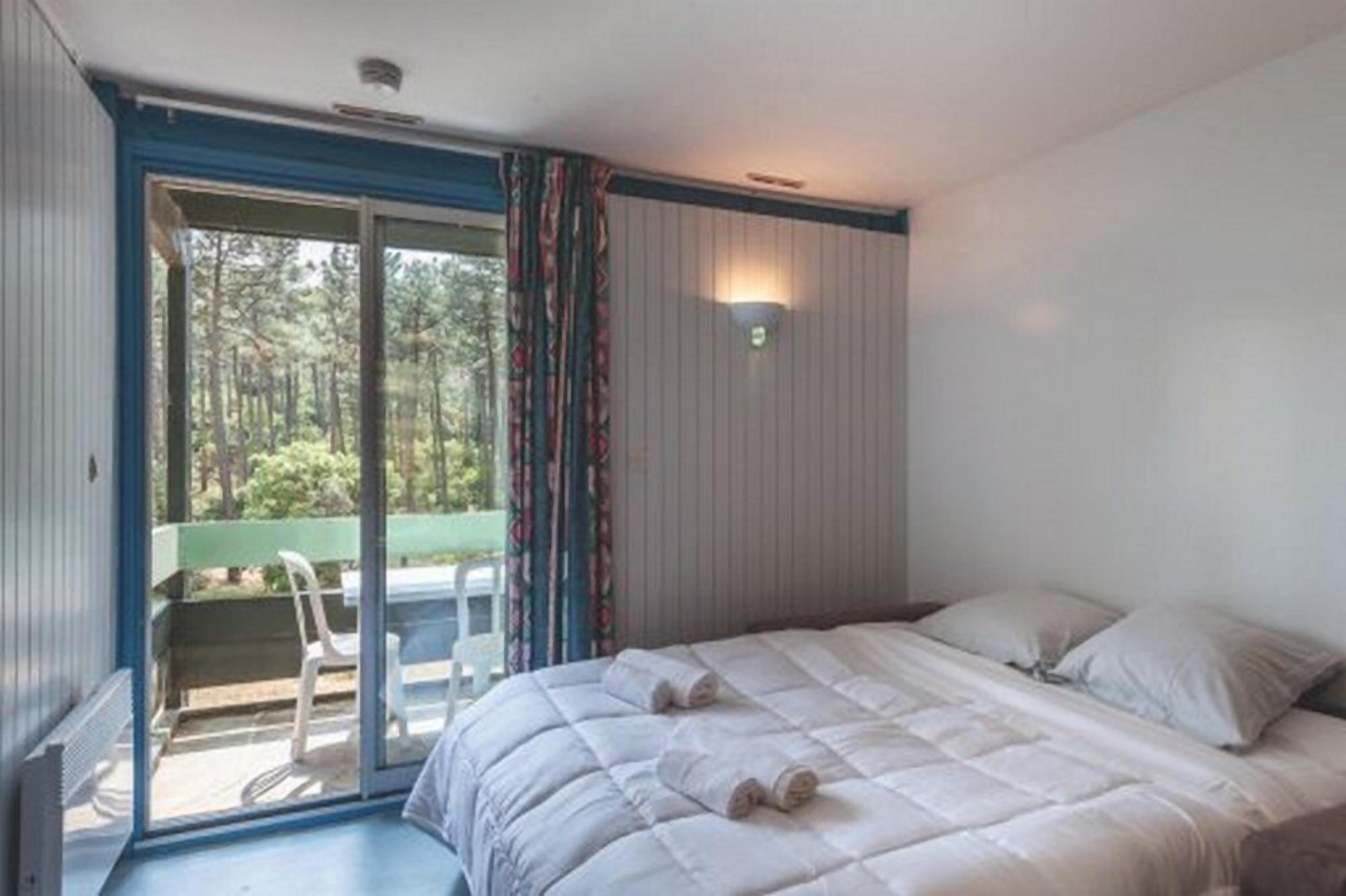 Un dormitorio con cama, puerta corrediza de vidrio que da a un balcón y una lámpara fijada a la pared.