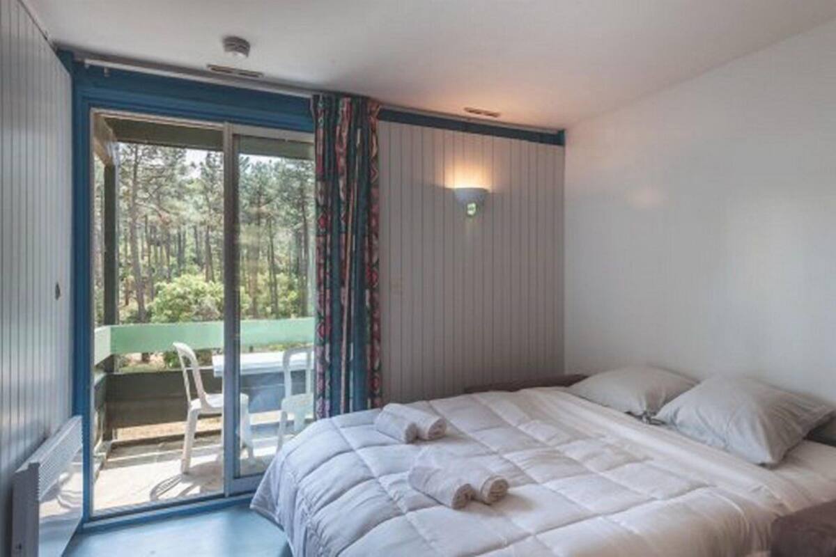 A bedroom with a bed, a sliding glass door leading to a balcony, and a wall-mounted light fixture.