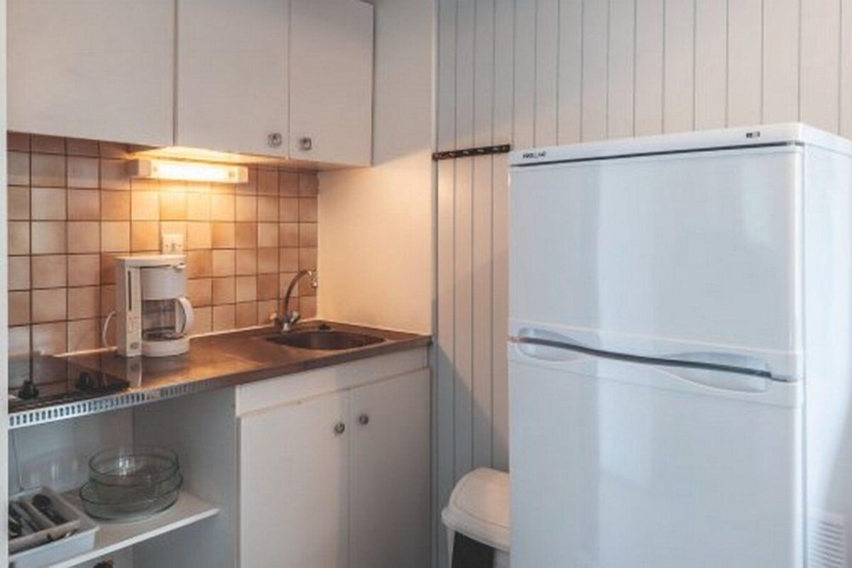 A compact kitchen with white cabinets, a built-in sink, a coffee maker, and a white refrigerator.