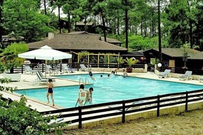 A swimming pool with lounge chairs and umbrellas, surrounded by trees and buildings. - Sowell LES Cavales (Carcans)