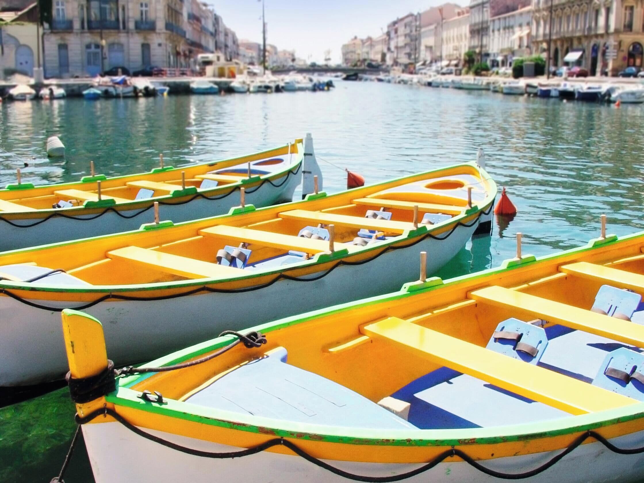 A row of colorful rowboats docked at a marina with buildings in the background.