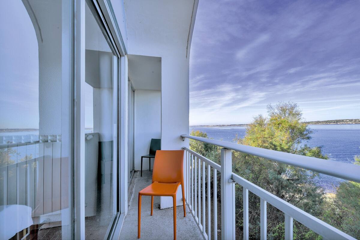 A balcony with a chair, a glass door, and a view of the sea.