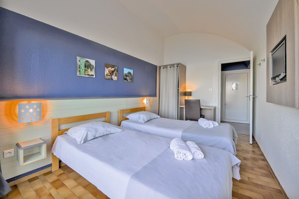 A hotel room with two beds, a nightstand, a desk, and a TV.