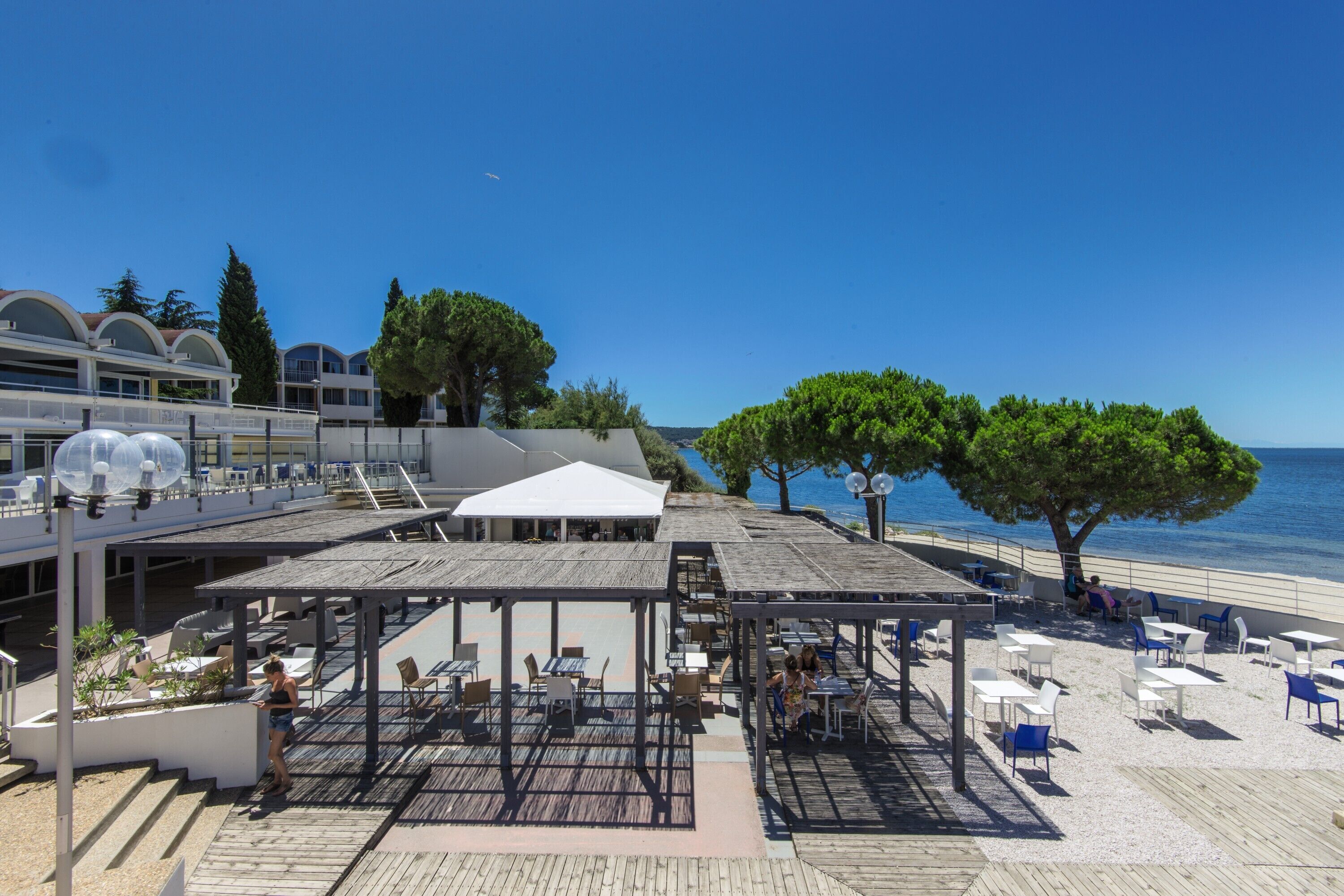 A seaside terrace with outdoor seating, a pool, and a view of the sea.