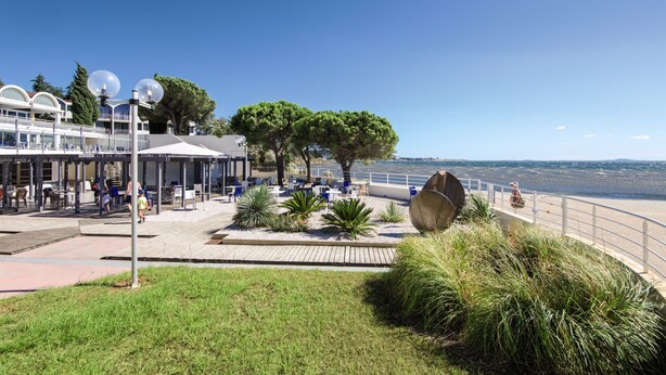 Un paseo marítimo con mesas al aire libre, una gran escultura decorativa y vista al mar.