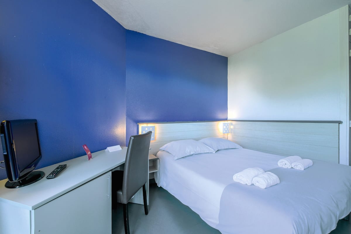 A hotel room with a bed, a desk with a computer, a chair, and a TV.