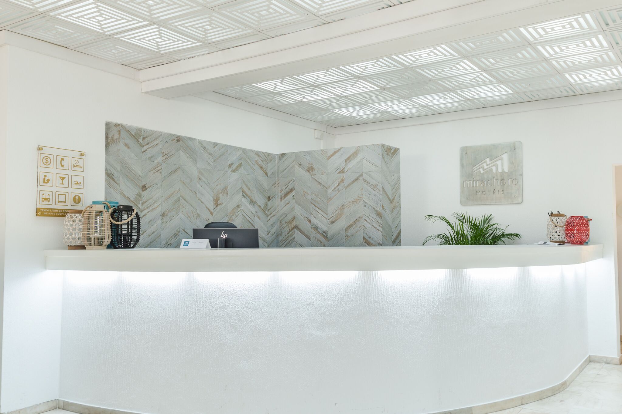 A reception desk with a herringbone-patterned wall, a framed sign with icons, and a plant on the right.