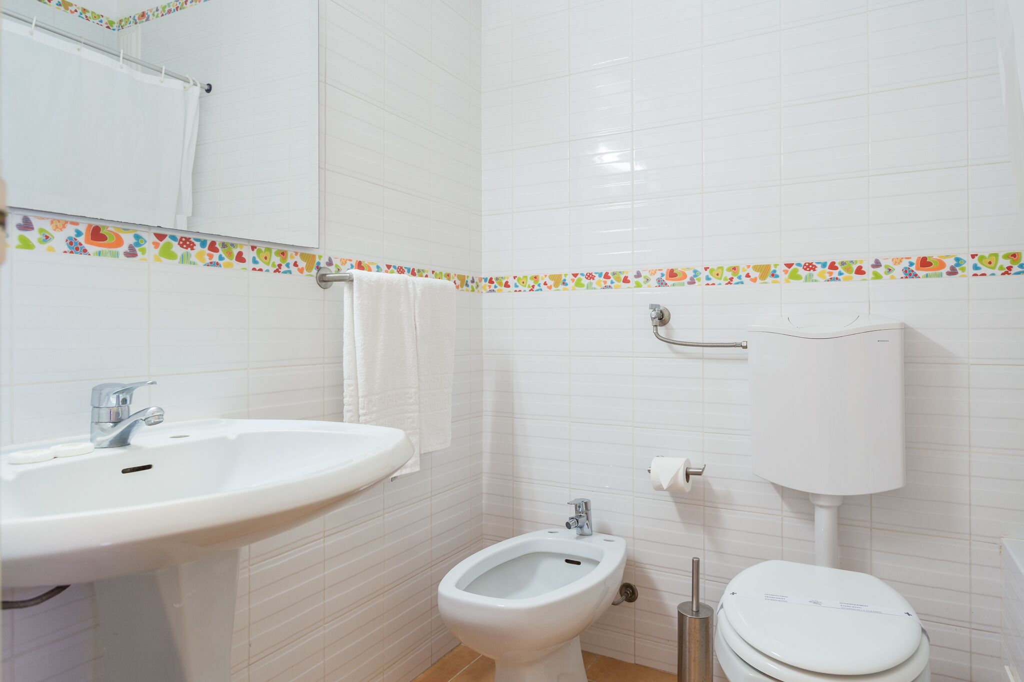 Une salle de bain équipée d’un lavabo, d’un bidet, de toilettes et de murs carrelés.