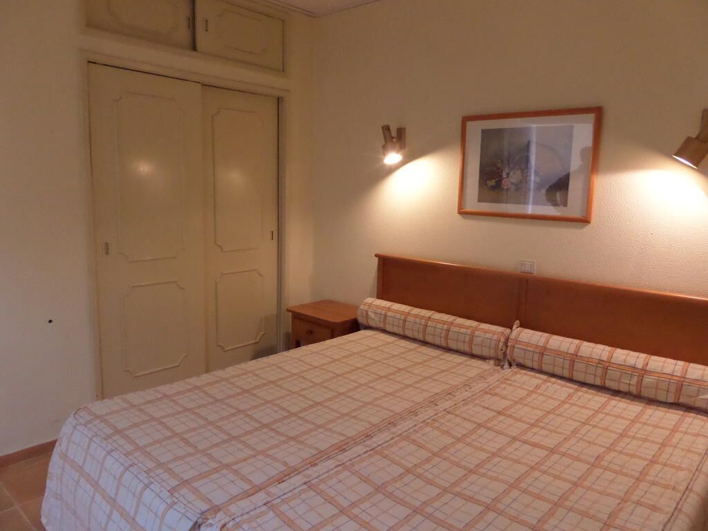 A bedroom with a bed, a nightstand, a framed picture on the wall, and a door.