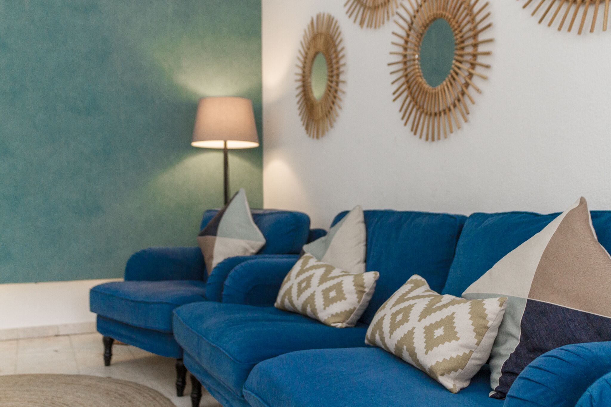 Een blauwe bank met gekleurde kussens, een vloerlamp en decoratieve spiegelwand.