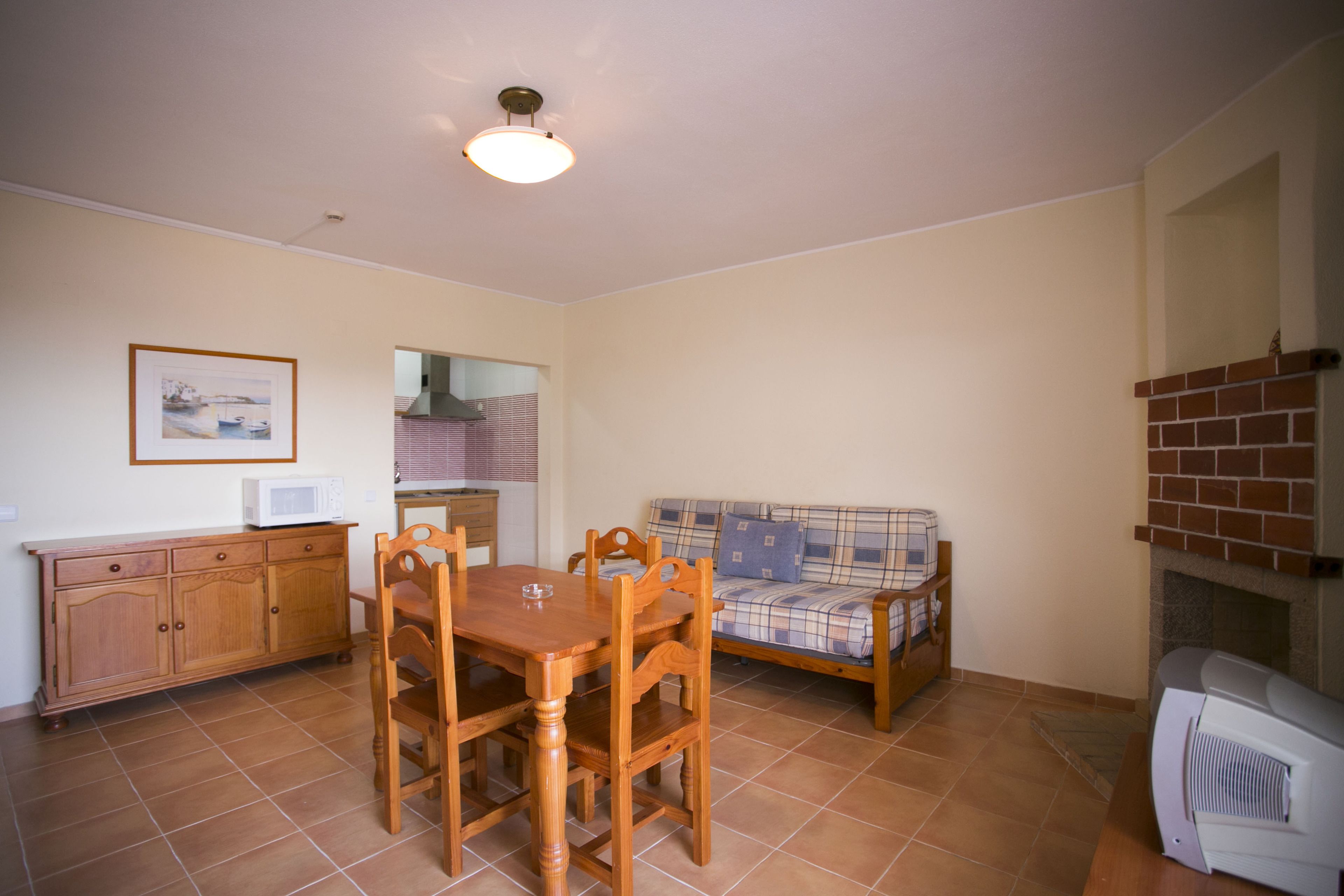 A dining area with a wooden table and chairs, a sofa, a microwave, and a fireplace.