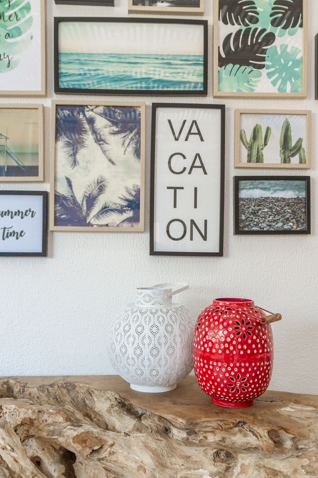 Eine Wand mit verschiedenen gerahmten Kunstwerken, darunter ein auffälliges 'VACATION'-Schild, und zwei dekorative Vasen auf einer Holzoberfläche.