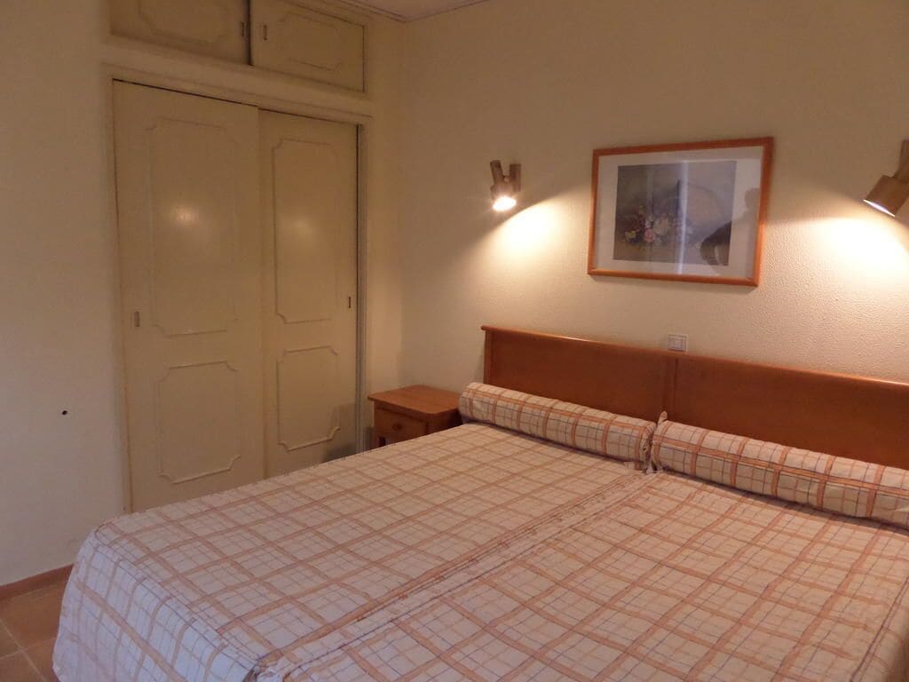 A bedroom with a bed, a nightstand, a framed picture on the wall, and a door.