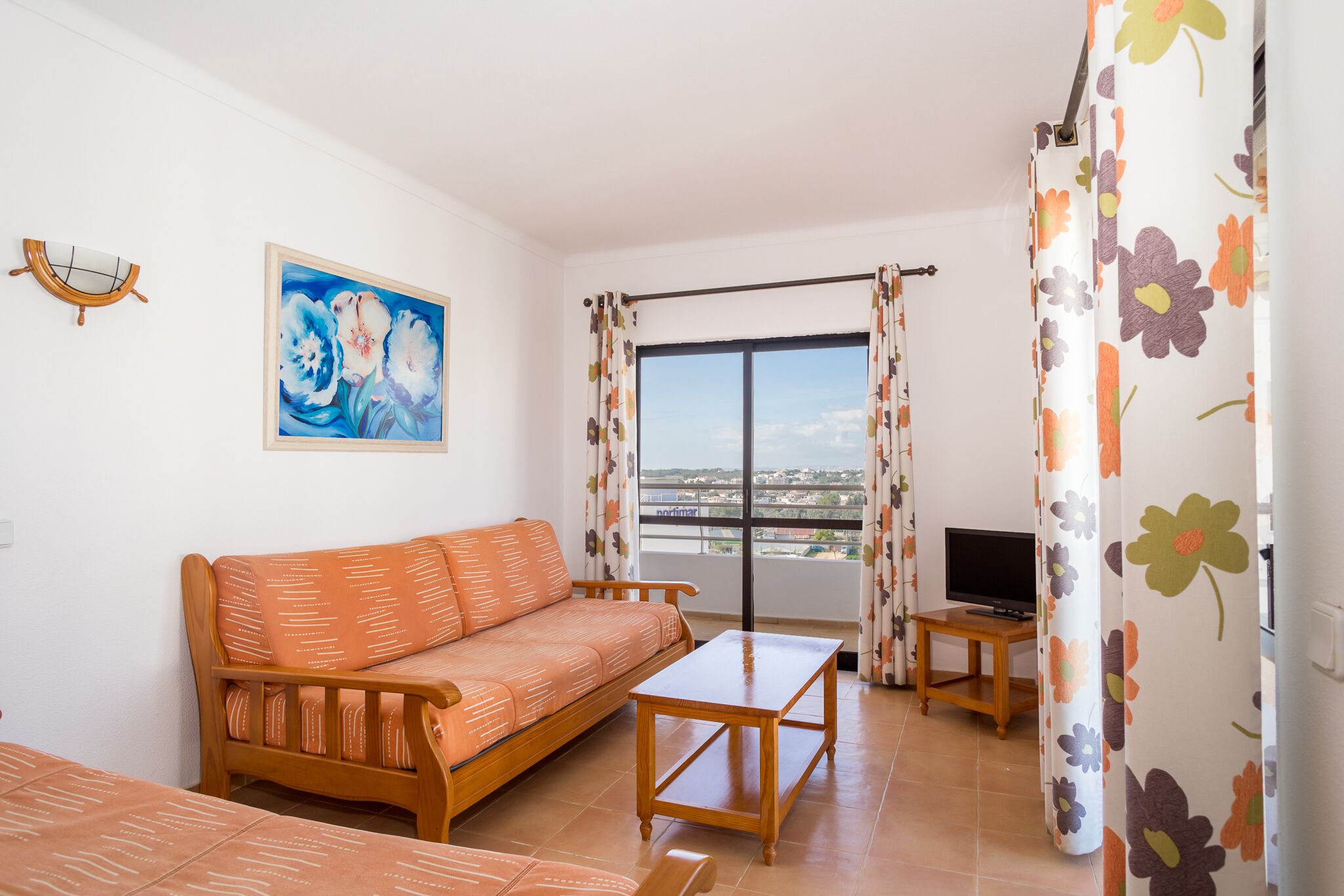 Una sala de estar con sofá, mesa de centro, televisor en un mueble bajo y balcón con vistas.