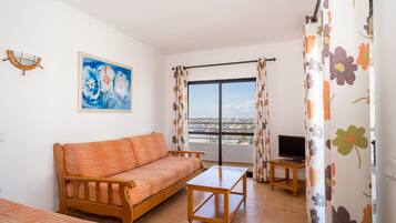 Una sala de estar con sofá, mesa de centro, televisor en un mueble bajo y balcón con vistas.