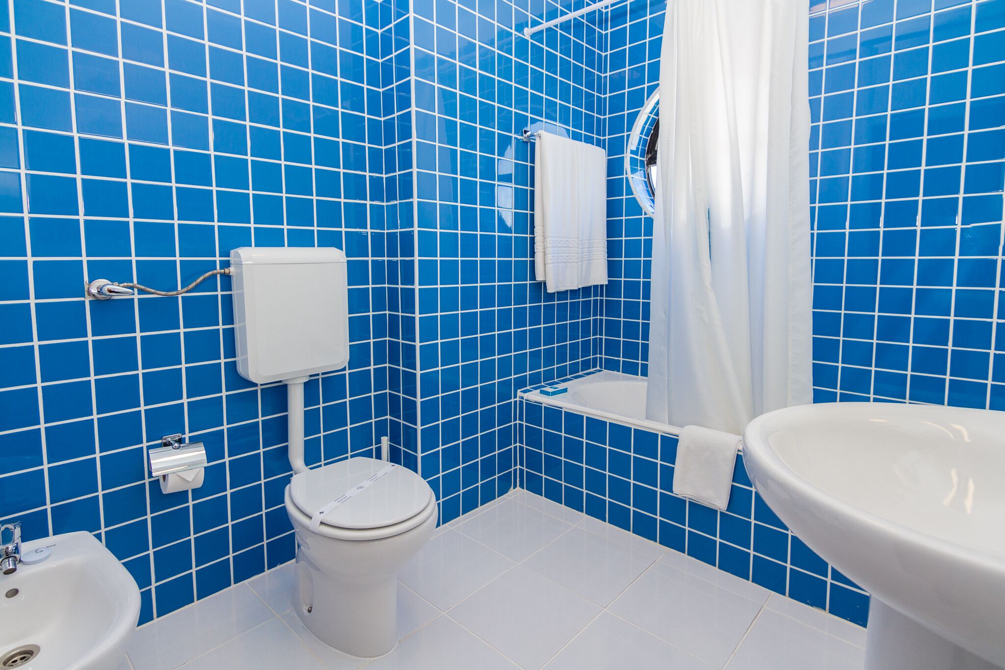 A bathroom with blue tiled walls, a white toilet, a sink, and a shower area.