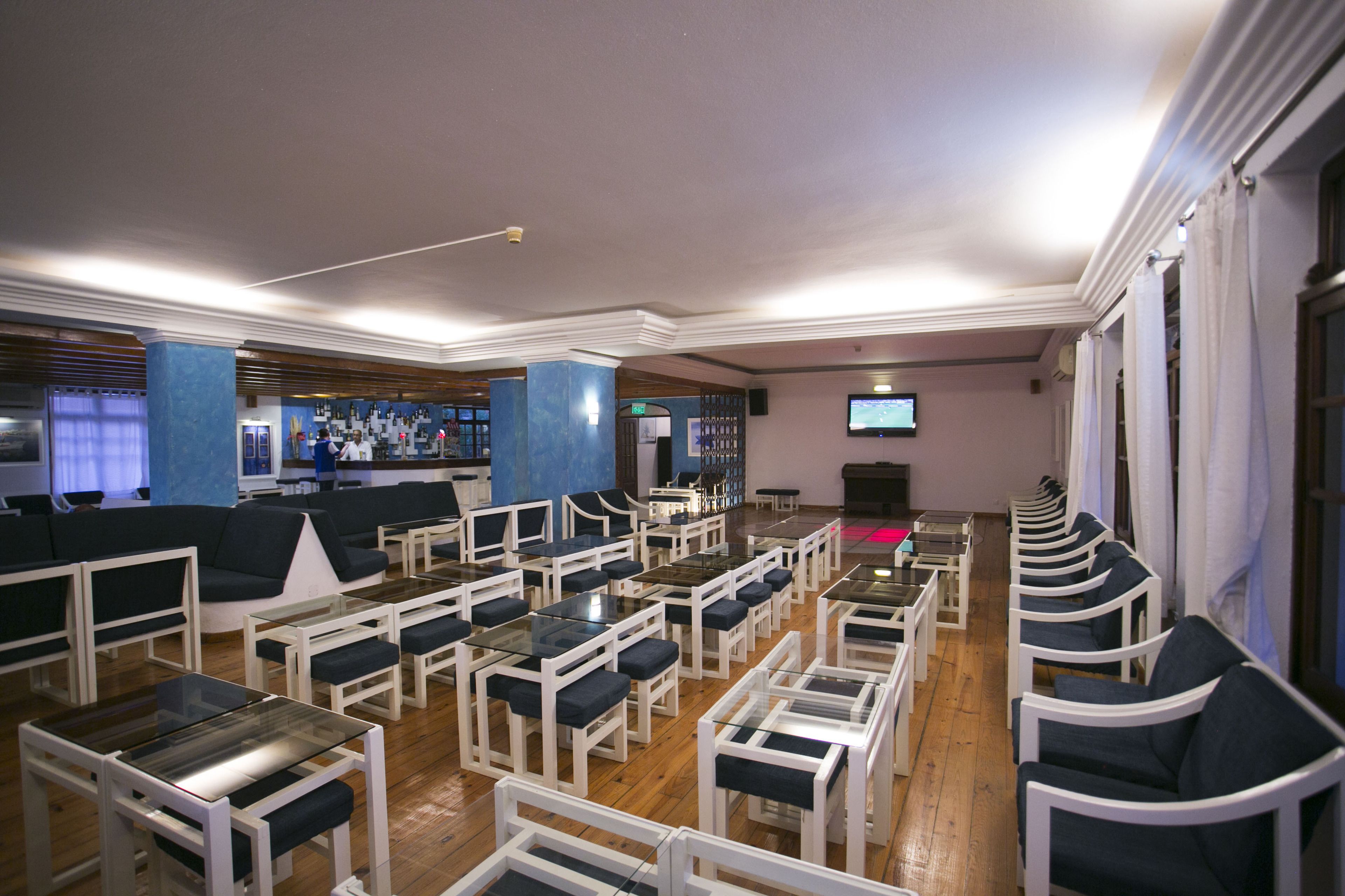 A hotel lobby with rows of seating, a bar area, and a television screen.