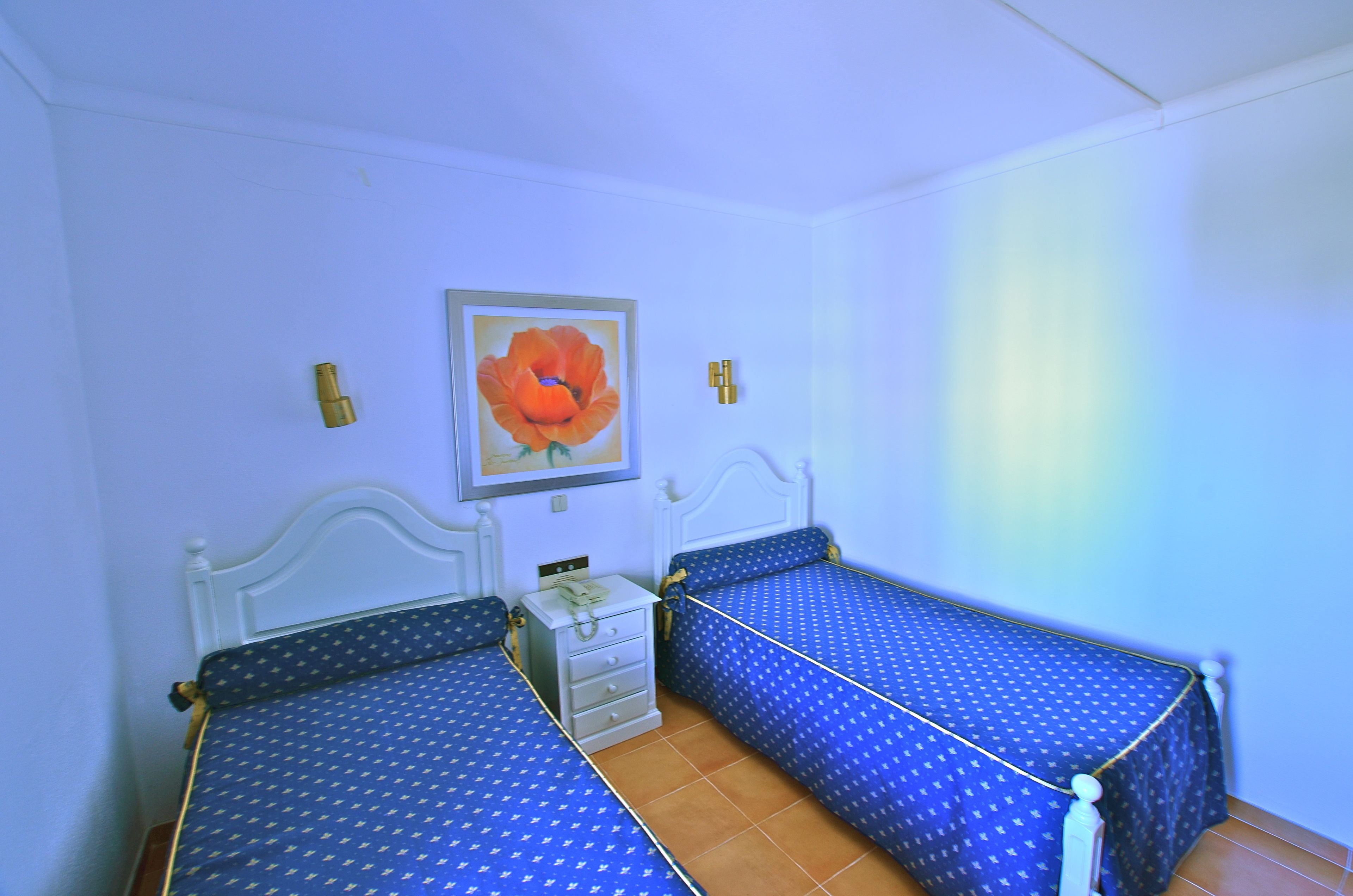 Une chambre avec deux lits, une table de chevet et un tableau encadré au mur.