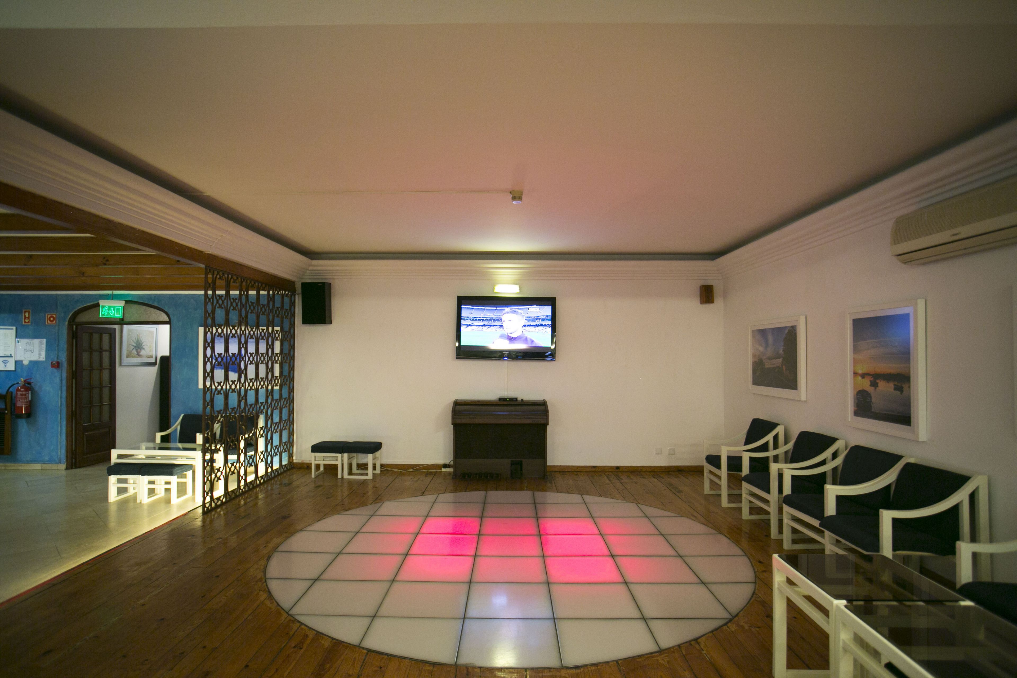 A room with a circular dance floor, a television mounted on the wall, and several chairs arranged around the room.