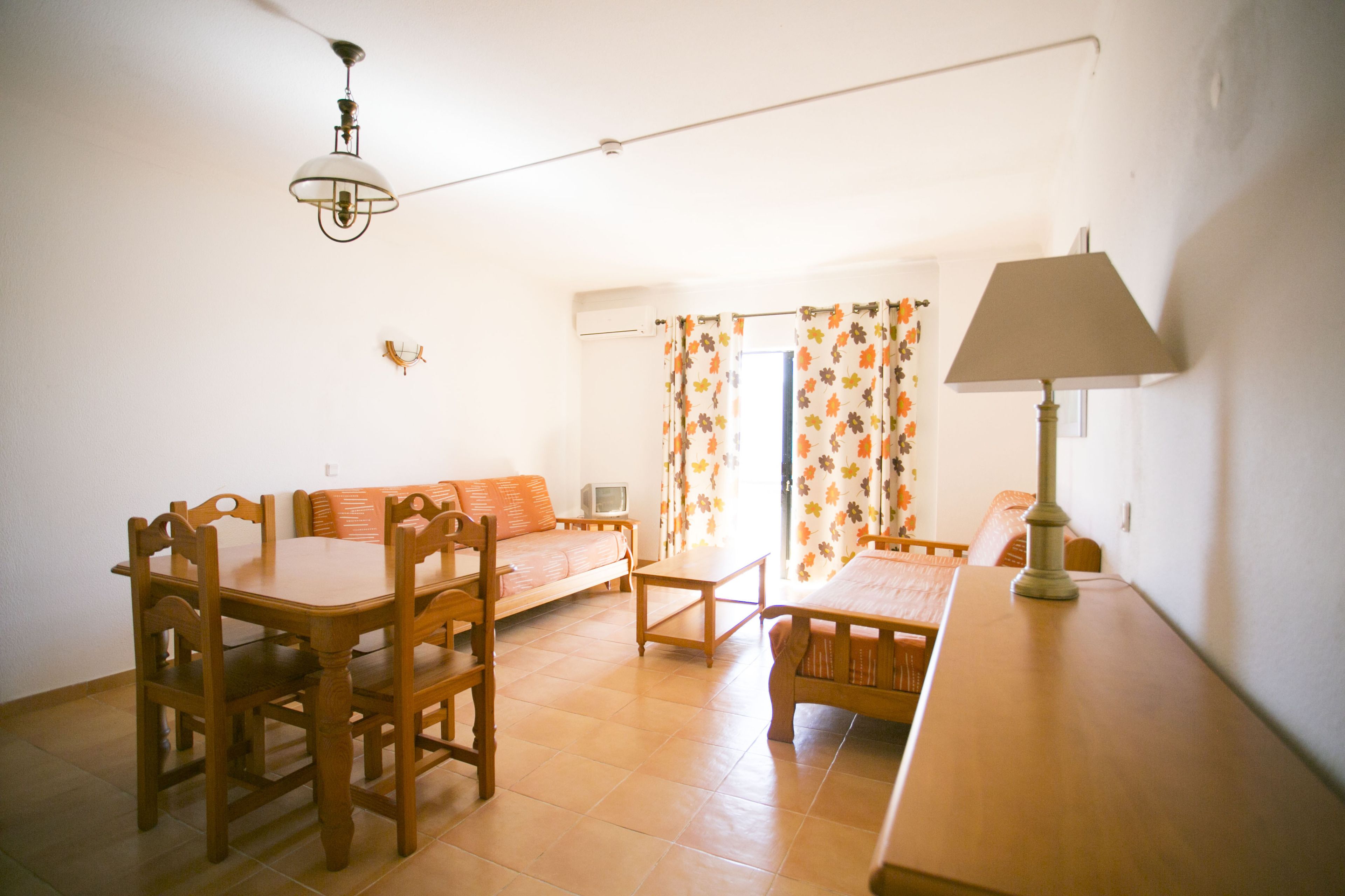 Ein Wohnzimmer mit Esstisch, Stühlen, einer Couch, einer Lampe und einem Fernseher.
