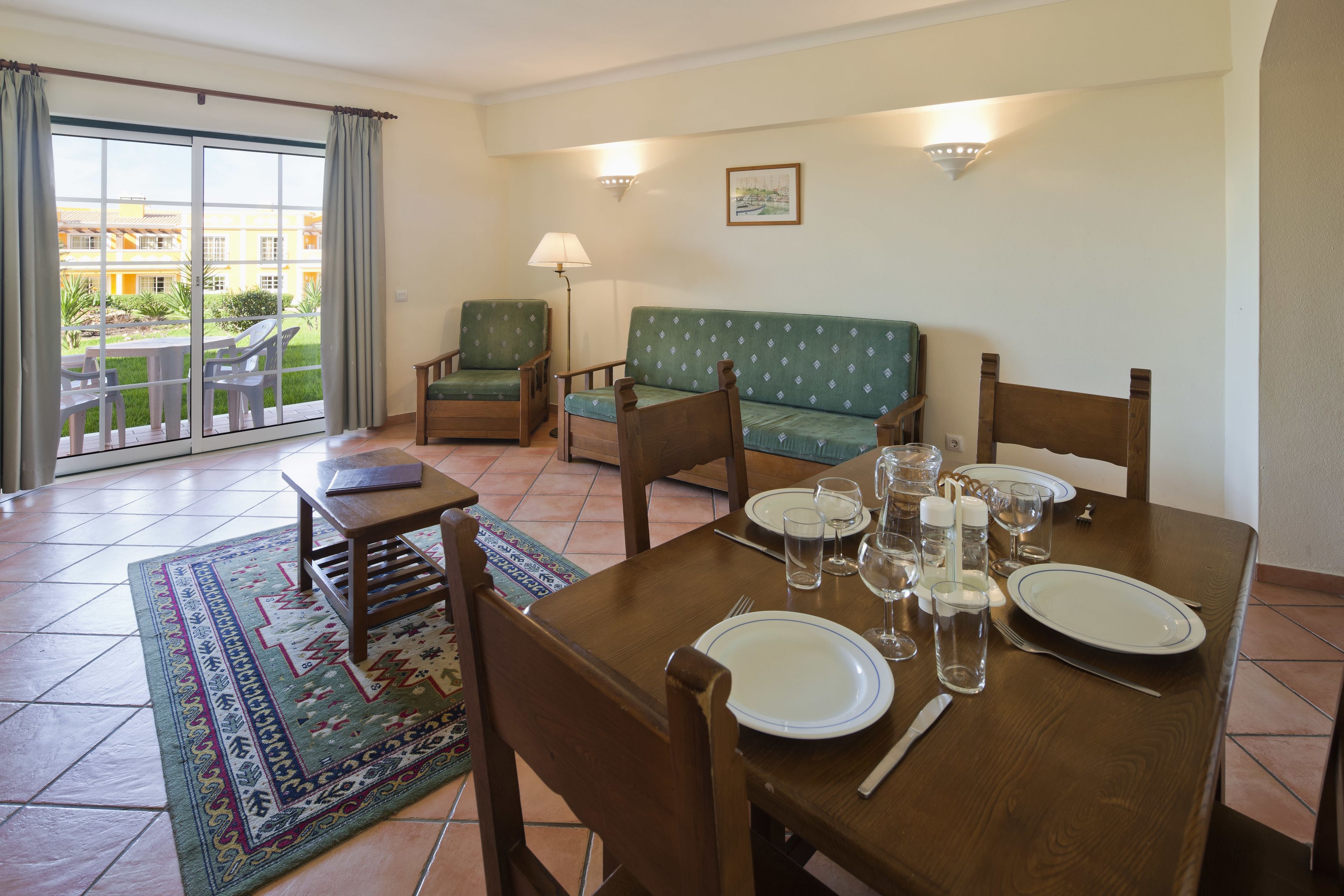 Un comedor con una mesa dispuesta para cuatro, sillas, un sofá y vistas a un patio a través de un puerta corredera.
