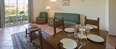 Un comedor con una mesa dispuesta para cuatro, sillas, un sofá y vistas a un patio a través de un puerta corredera.