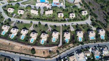 An aerial view of a residential area with multiple houses, roads, and a large swimming pool.