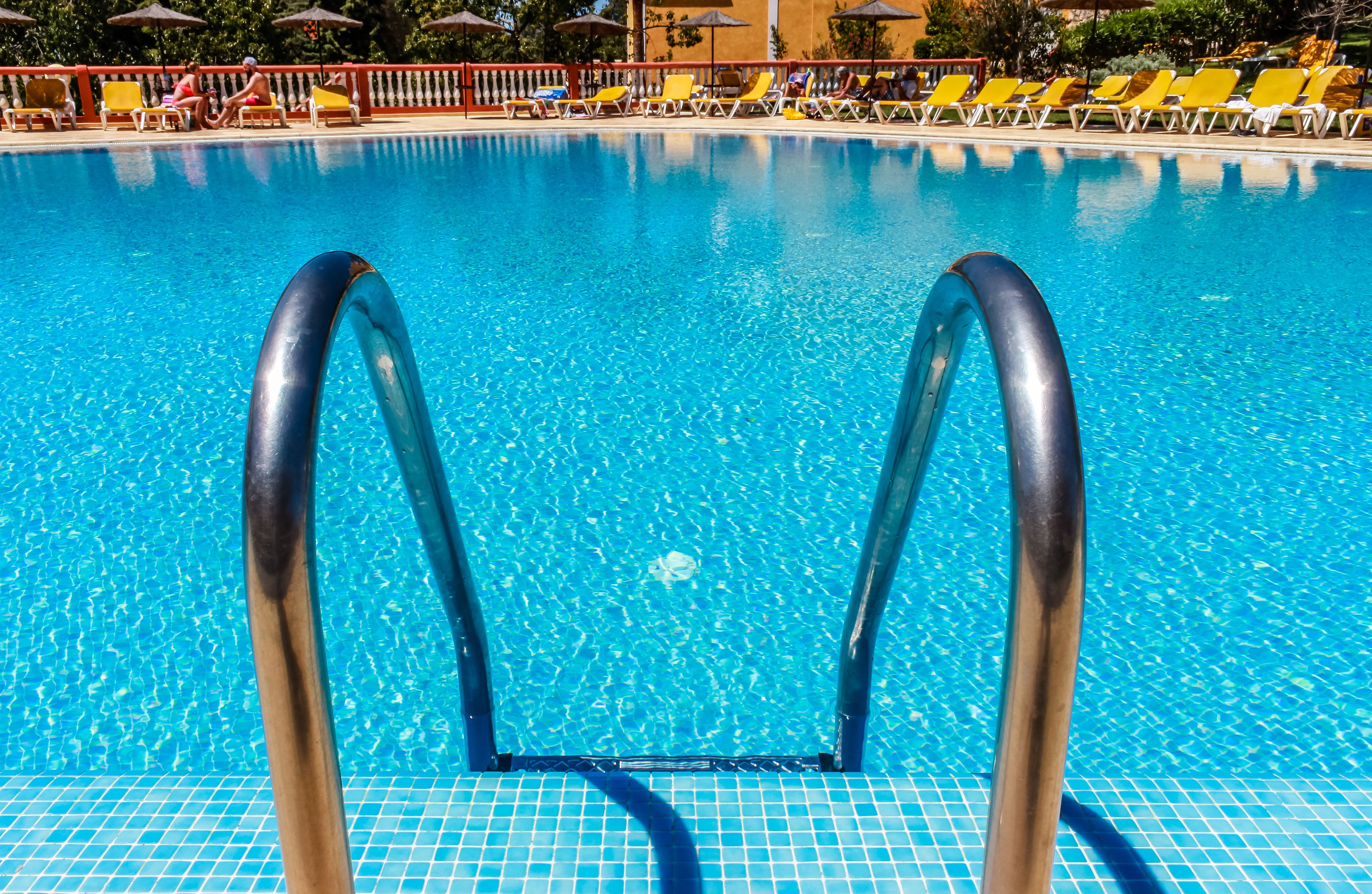 Une piscine à l’eau d’un bleu cristallin, des chaises longues jaunes et une terrasse carrelée.