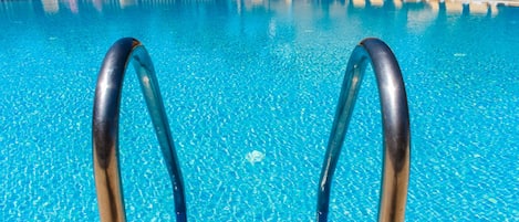Une piscine à l’eau d’un bleu cristallin, des chaises longues jaunes et une terrasse carrelée.