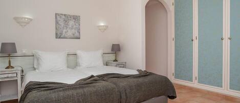 A bedroom with a bed, nightstands, wall sconces, a wardrobe, and a painting.