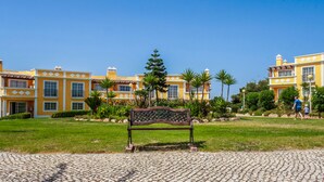 A courtyard with a bench, surrounded by yellow buildings with decorative windows and a clear blue sky. - Colina da Lapa & Villas (Lagoa)