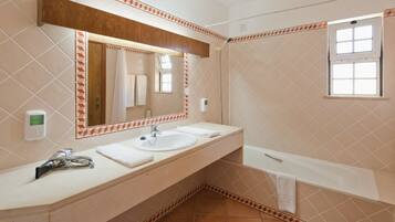 A bathroom with a double sink, a large mirror, a window, and a bathtub.