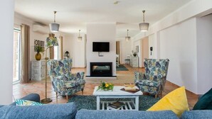A modern living room with a fireplace, two patterned armchairs, a sofa, and a coffee table. - Colina da Lapa & Villas (Lagoa)