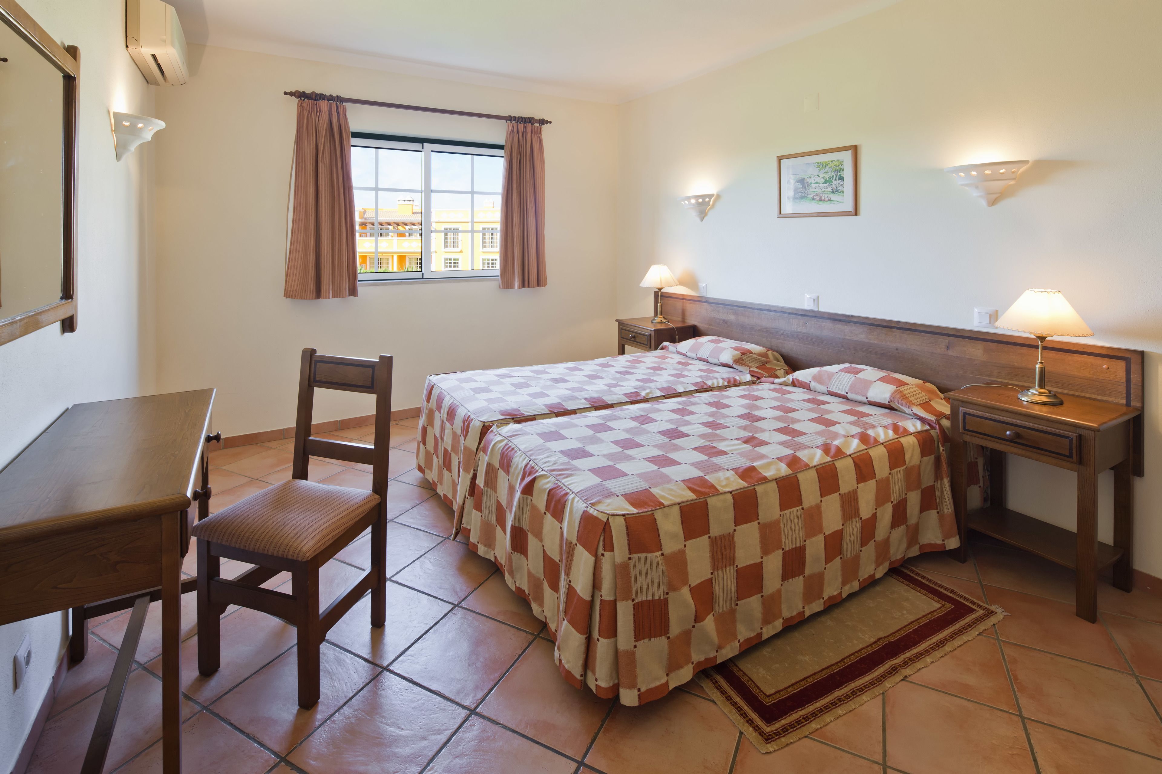 A hotel room with two beds, a desk, a chair, and a window with curtains.