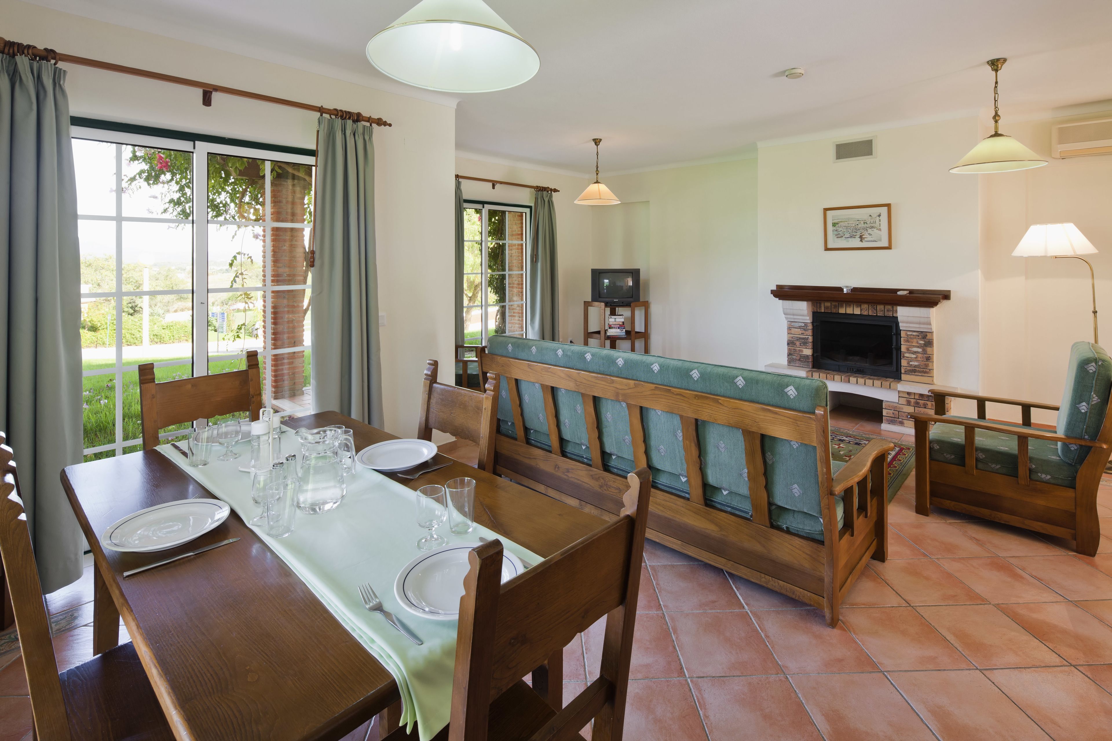 Un comedor con una mesa de madera dispuesta para cuatro personas, un banco con cojines y una chimenea.