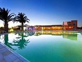 Una piscina de hotel con el reflejo de palmeras y un edificio con iluminación cálida.