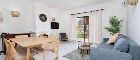 Un salón moderno con una mesa de comedor de madera, un sofá gris y un televisor montado en la pared.