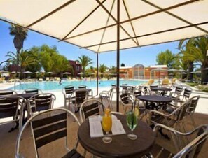 Un espace extérieur avec une piscine, des tables et des chaises sous des parasols, offrant une vue sur la piscine.
