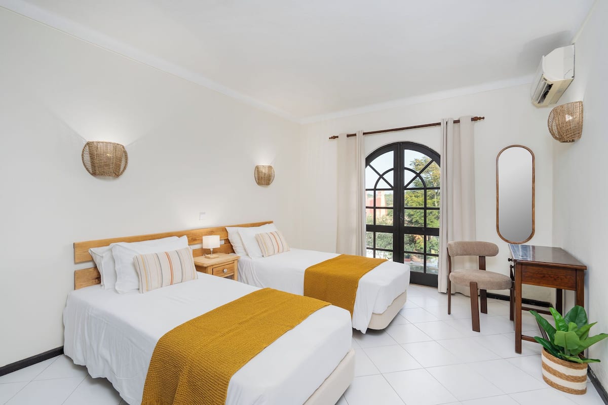Une chambre d’hôtel avec deux lits, un bureau, une chaise, un miroir et une fenêtre avec des rideaux.