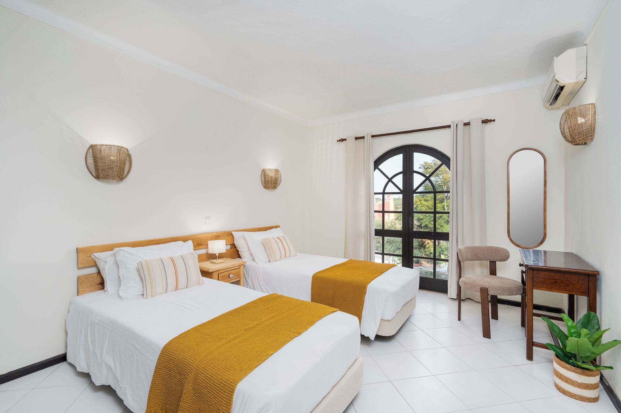 Une chambre d’hôtel avec deux lits, un bureau, une chaise, un miroir et une fenêtre avec des rideaux.