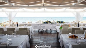 Zona pranzo all'aperto con tavoli apparecchiati per un pasto, con vista sul mare.