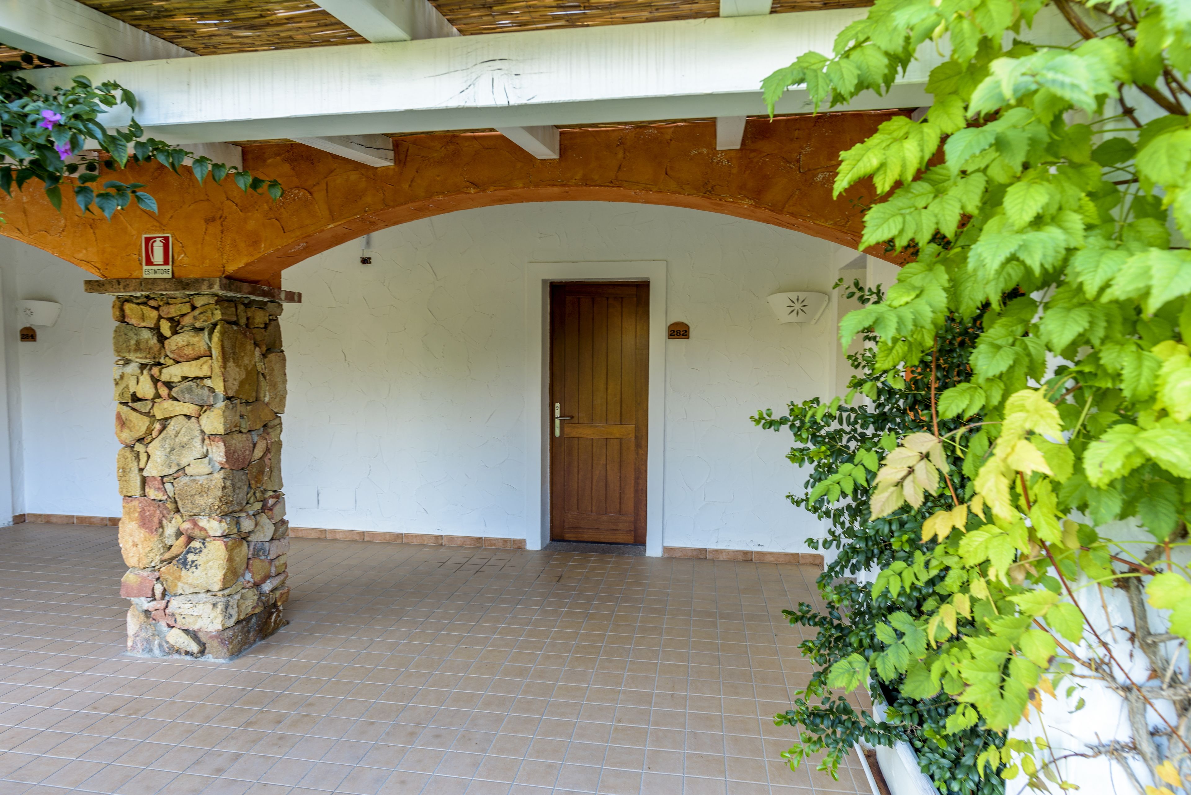A stone pillar, a wooden door, and a tiled floor in a covered outdoor area.