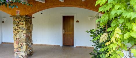 A stone pillar, a wooden door, and a tiled floor in a covered outdoor area.