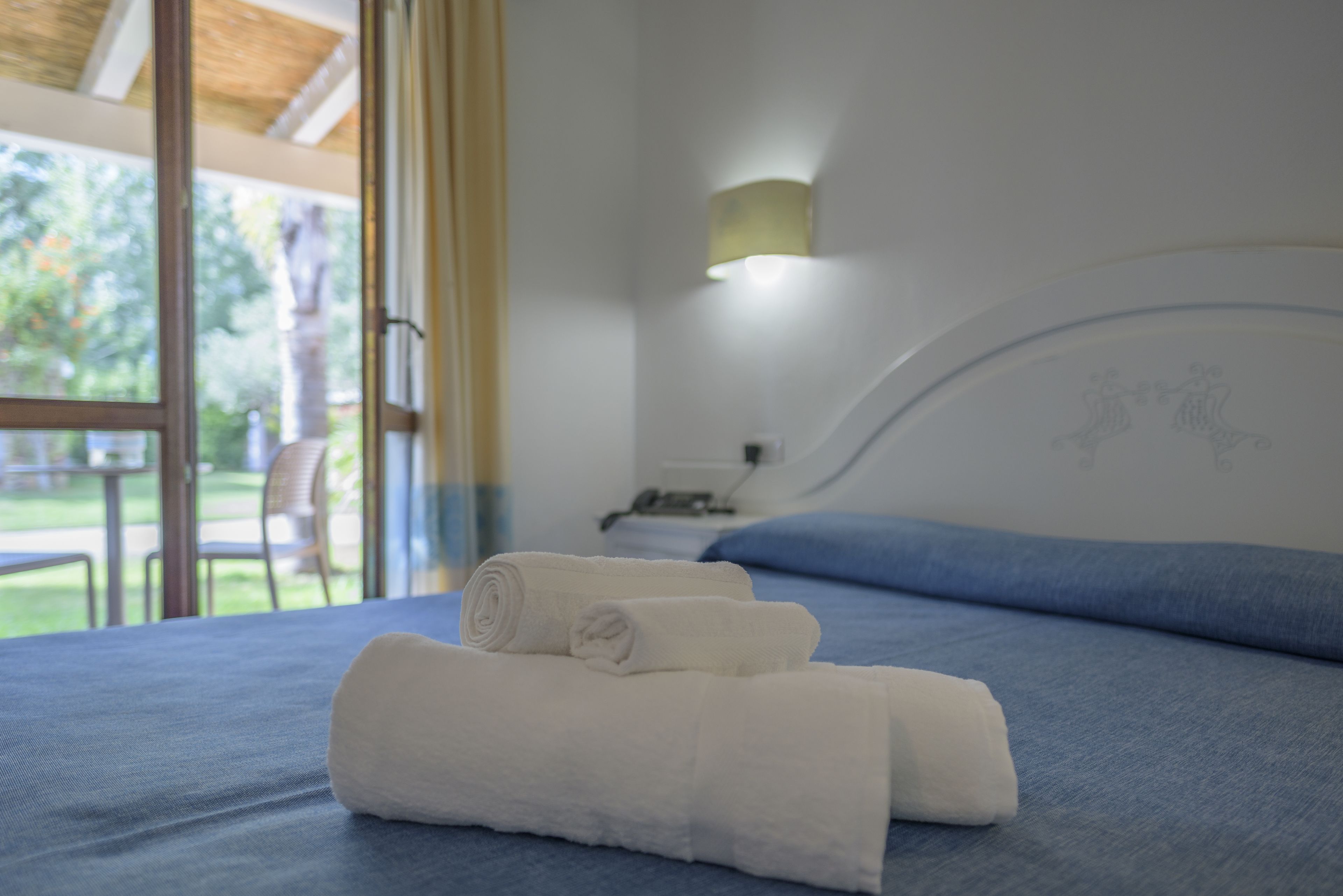 A neatly made bed with blue bedding and two rolled white towels.
