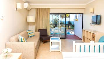 A hotel room with a sofa, armchair, TV, and a view of a pool and outdoor area.