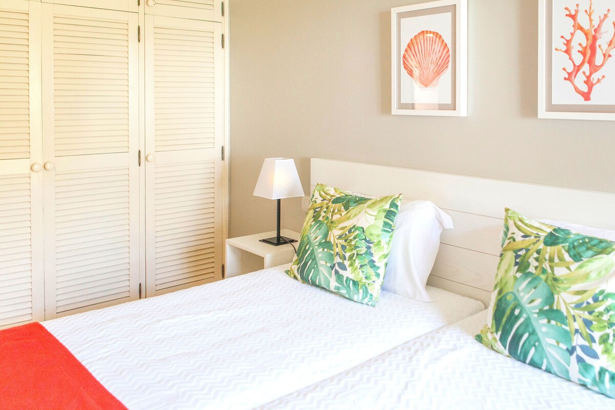 A hotel room with a bed, a nightstand, a lamp, and two framed pictures on the wall.
