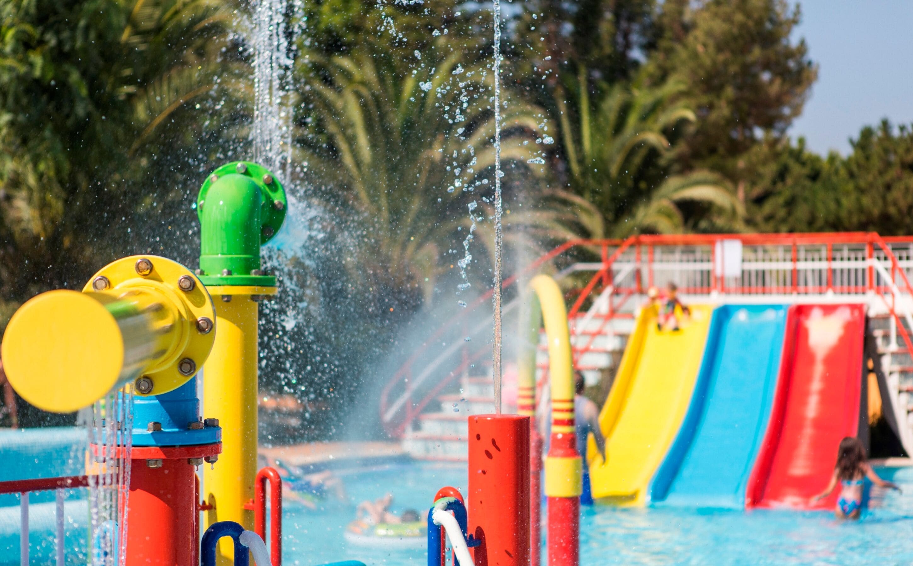 Een waterpark met een zwembad, glijbanen en fonteinen.