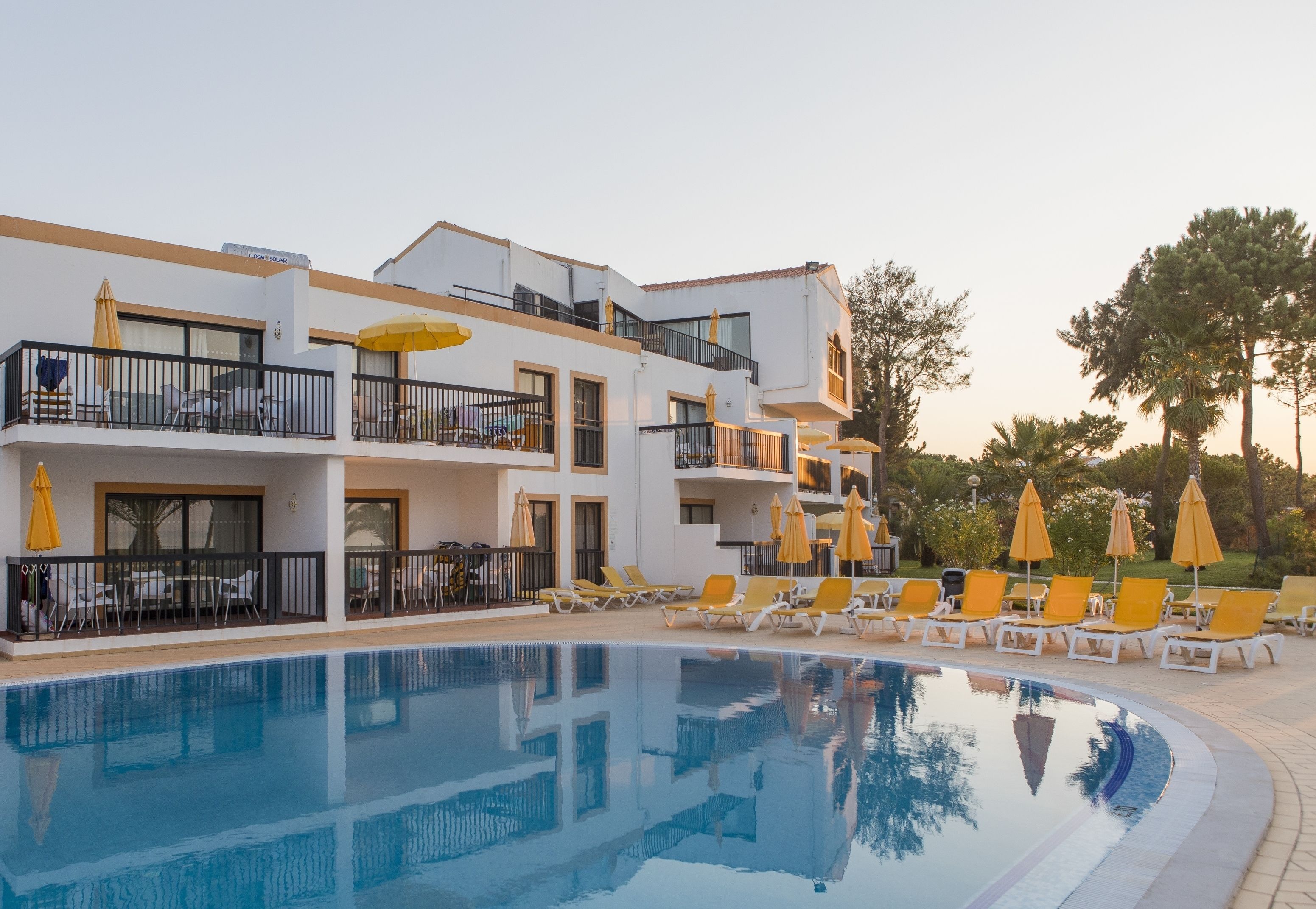 A modern hotel with a swimming pool, sun loungers, and outdoor seating.