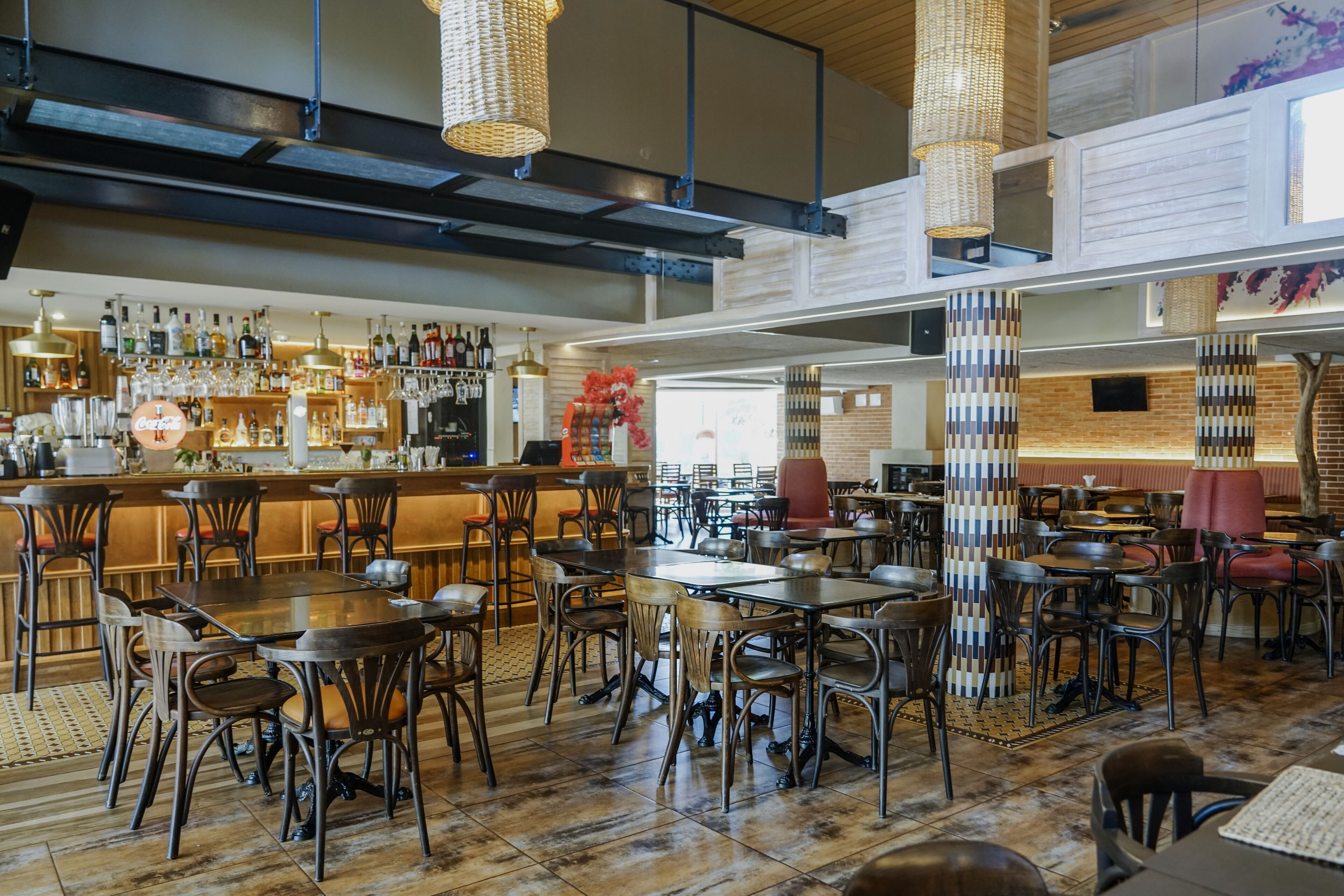A spacious restaurant with multiple dining tables and chairs, a bar area with a variety of bottles, and a modern interior design.